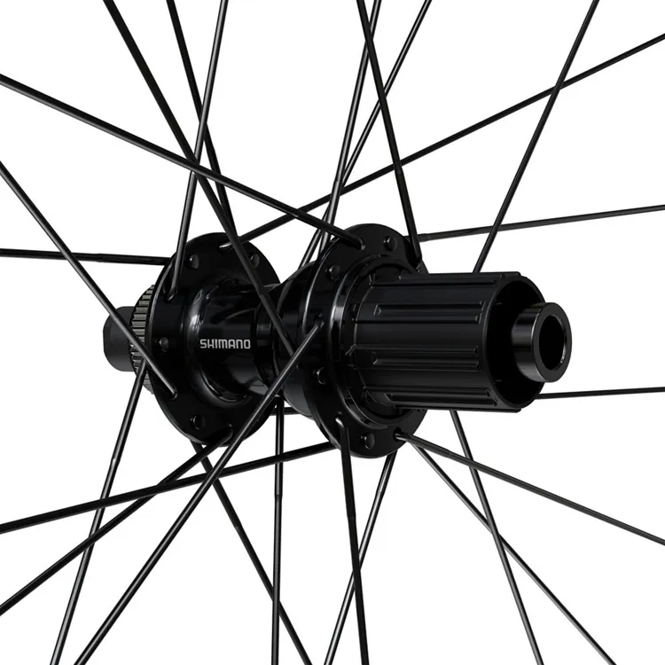 Primer plano del buje trasero Shimano de la rueda RX180, con radios negros distribuidos en patrón cruzado. El diseño permite el uso de núcleos HGL y Micro Spline, optimizando la compatibilidad con distintas transmisiones para gravel.