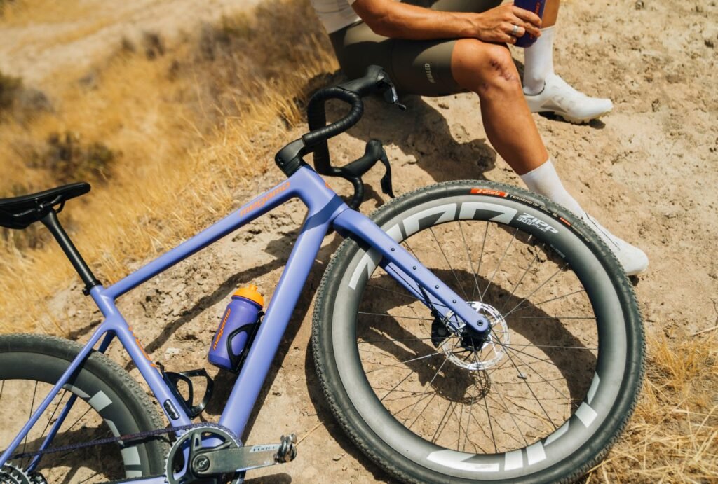 Bicicleta Megamo West 2026 en acción durante una salida gravel, con ciclista descansando junto al camino y paisaje seco.