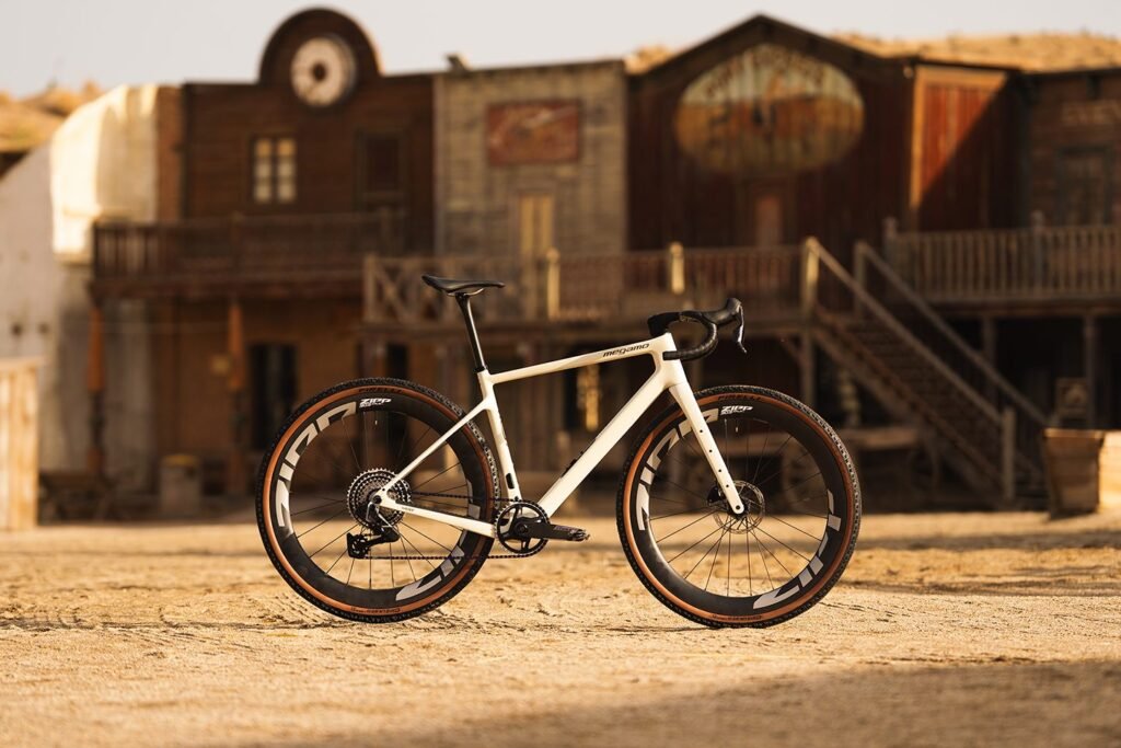Bicicleta Megamo West MY26 en color Sand con ruedas Zipp, fotografiada en un entorno tipo western, destacando su diseño limpio y racing.