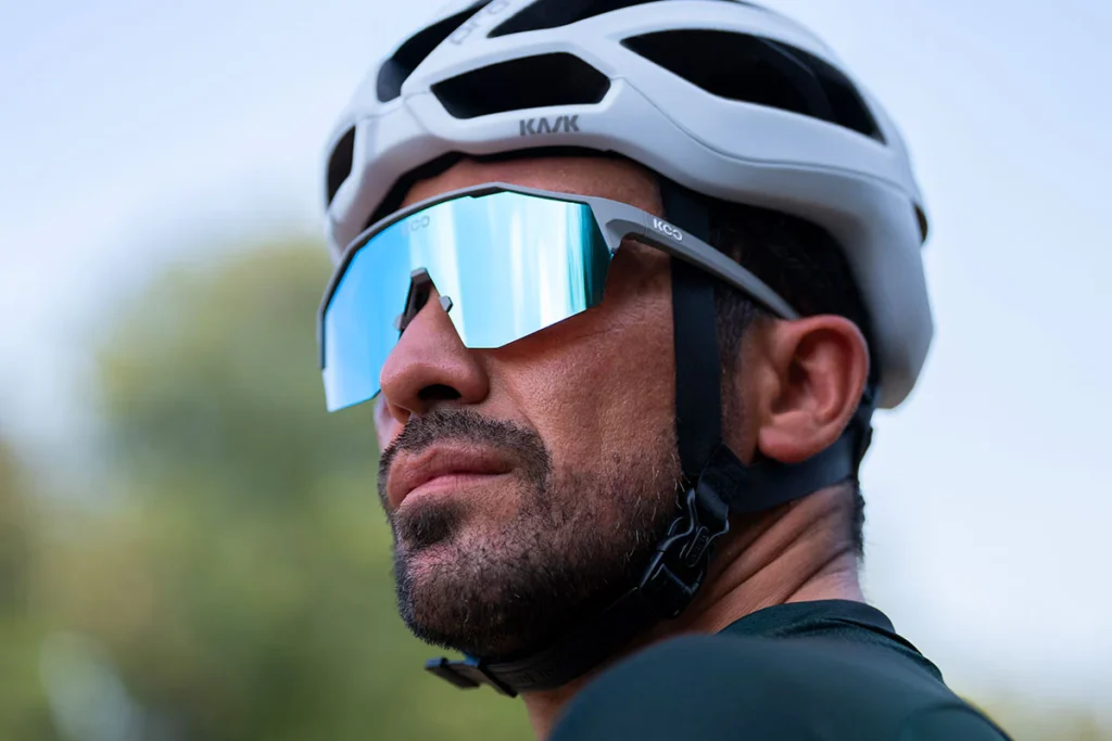 Primer plano de ciclista con gafas KOO Alibi Fuchsia Mirror reflejando el paisaje.